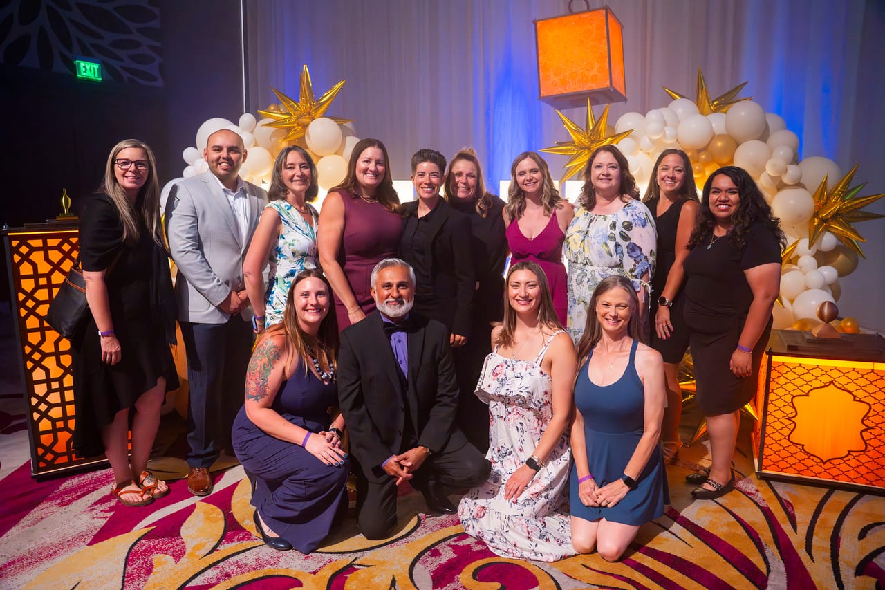 A big Renown team kneeling and standing together at the AMAZING arch