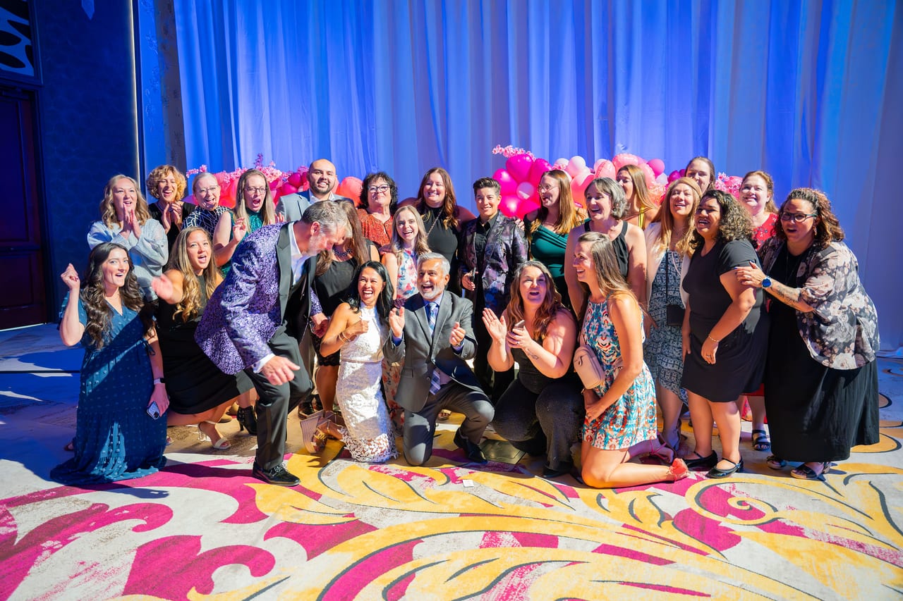 A big Renown team cheering and posing for a group photo in front of the stage