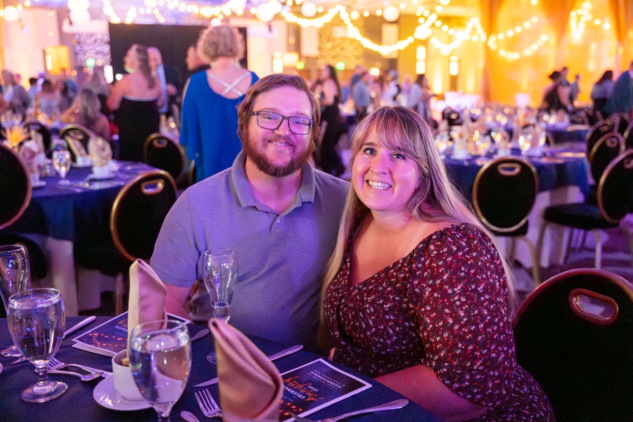 A Renown couple smiling at their table in the busy ballroom