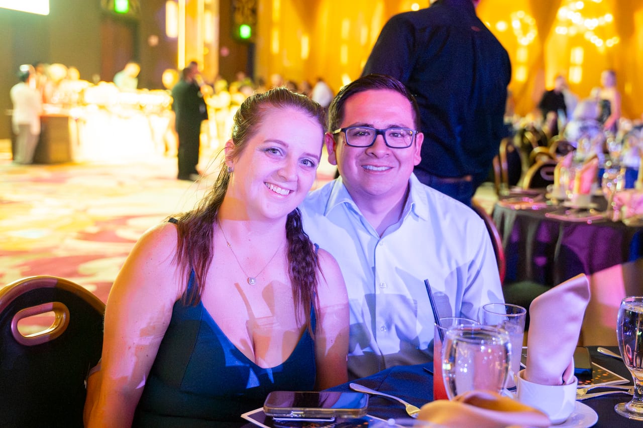 A Renown couple smiling at their table in the warm ballroom light