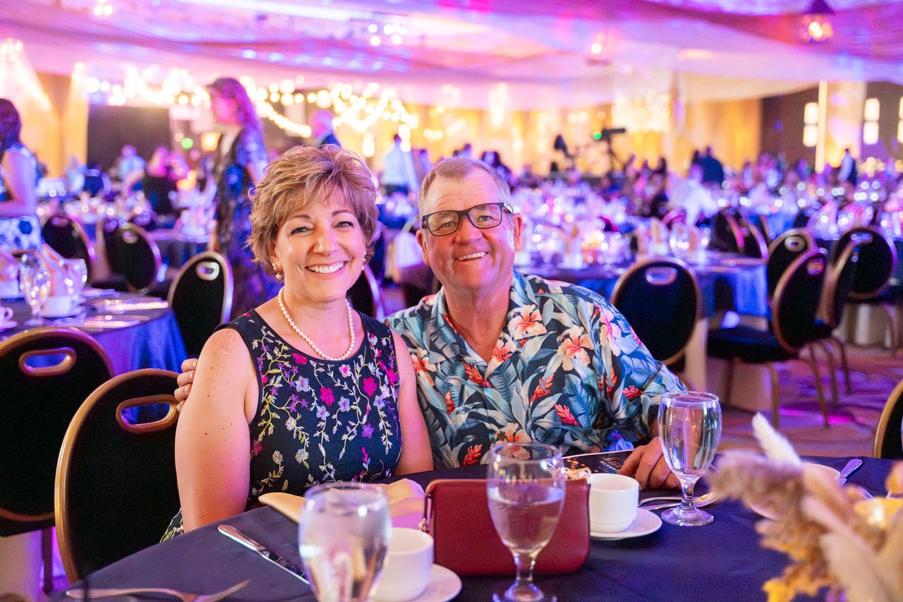 A Renown couple smiling at their table, him in a floral Hawaiian shirt
