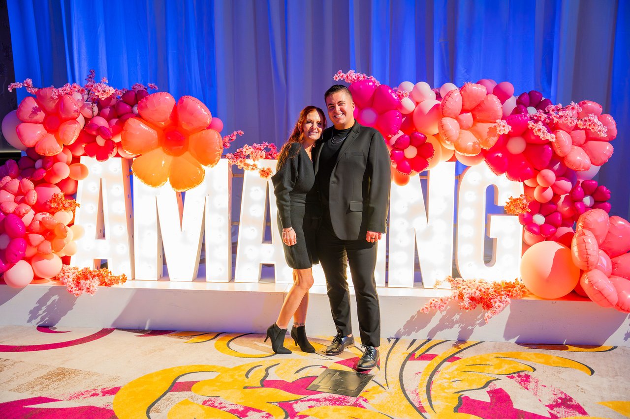 A Renown couple in black posing at the Amazing sign