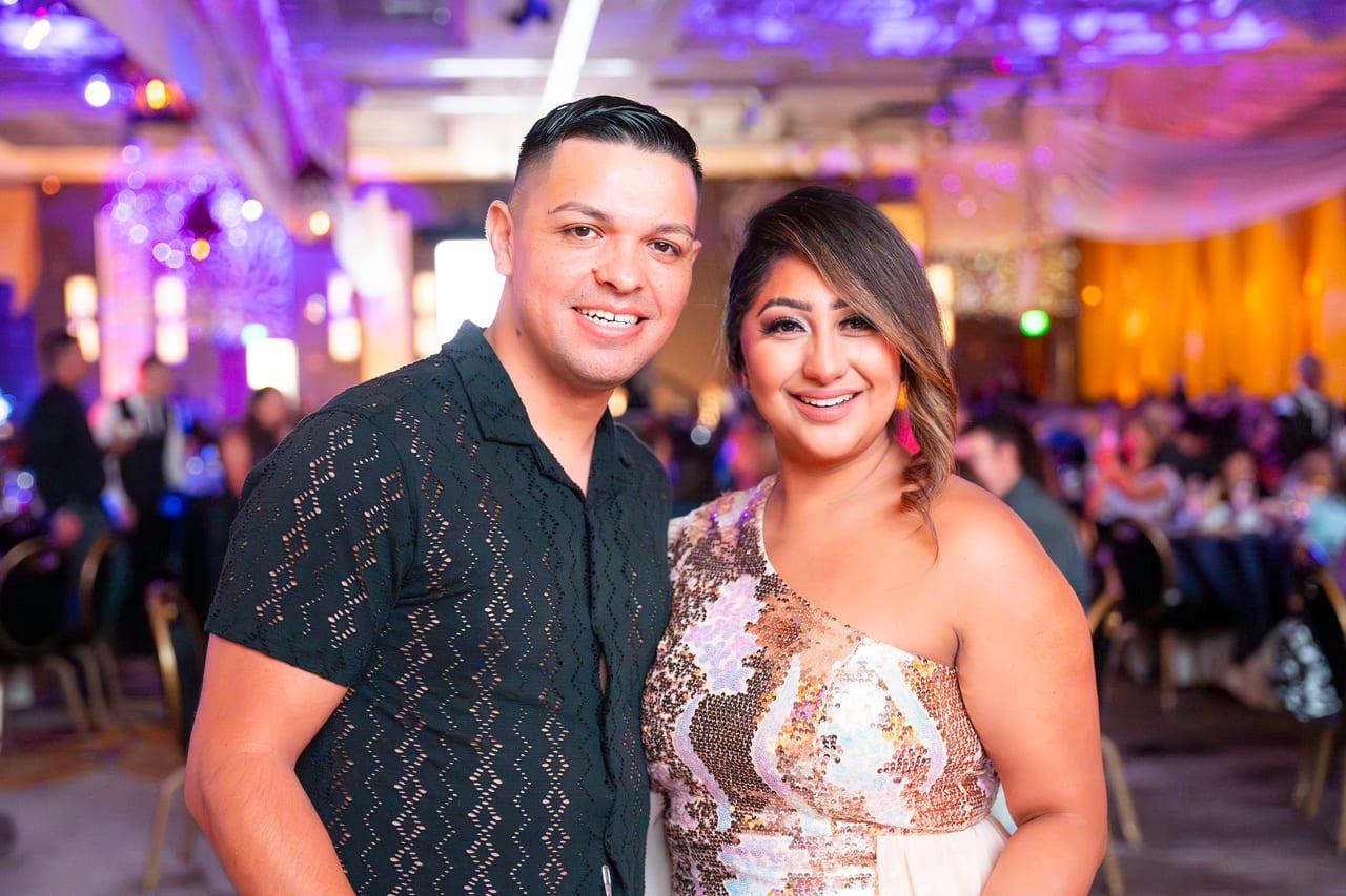 A Renown couple smiling in the ballroom, her in a rose gold sequined dress