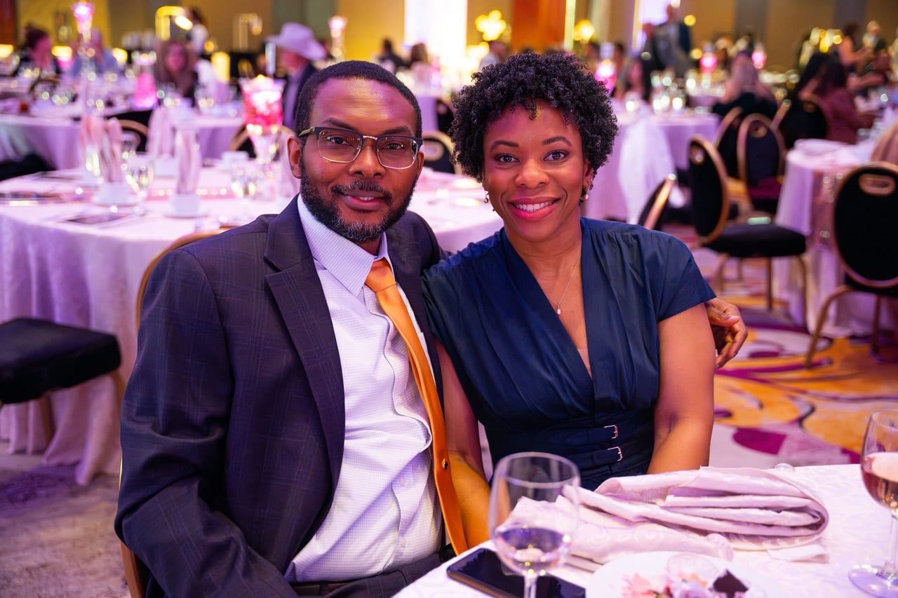 A Renown couple in a suit and a blue dress smiling at their table