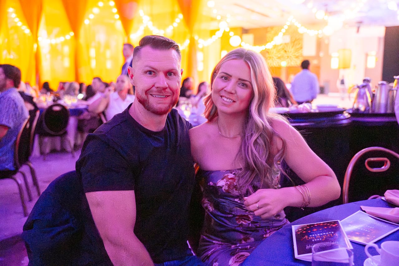 A Renown couple smiling at their table in the warm string light glow