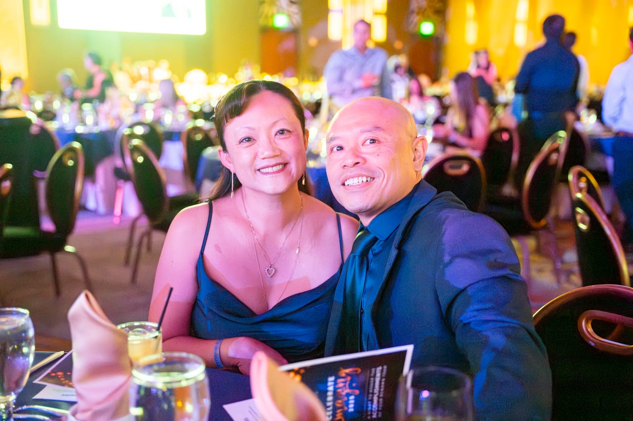 A Renown couple leaning in for a photo at their table