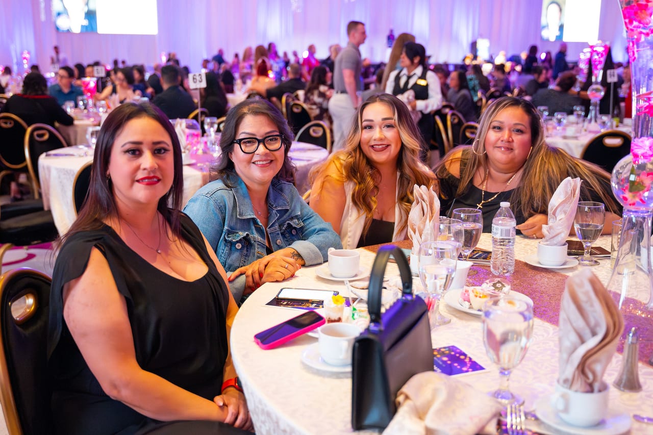 Four Renown coworkers smiling at their table with the ballroom full behind them