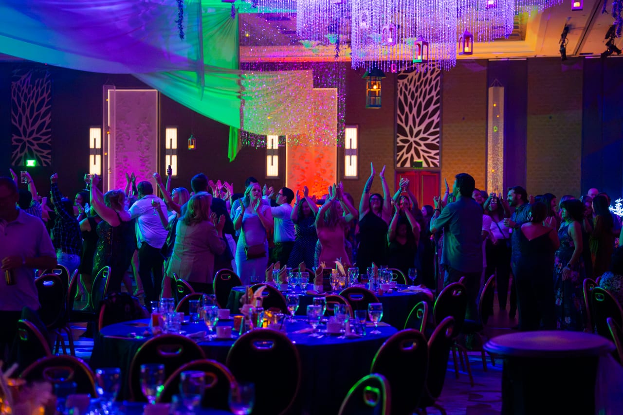 A crowd of Renown guests with their hands up on the dance floor beyond the tables