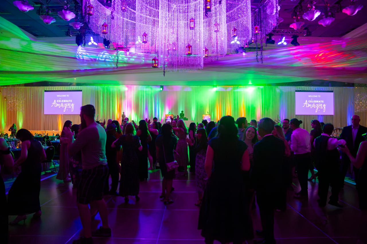 A packed dance floor under the chandelier and the Celebrate Amazing screens