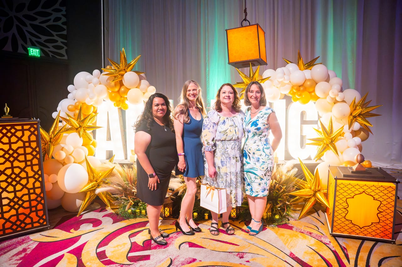 Four Renown friends posing together at the gold star balloon arch