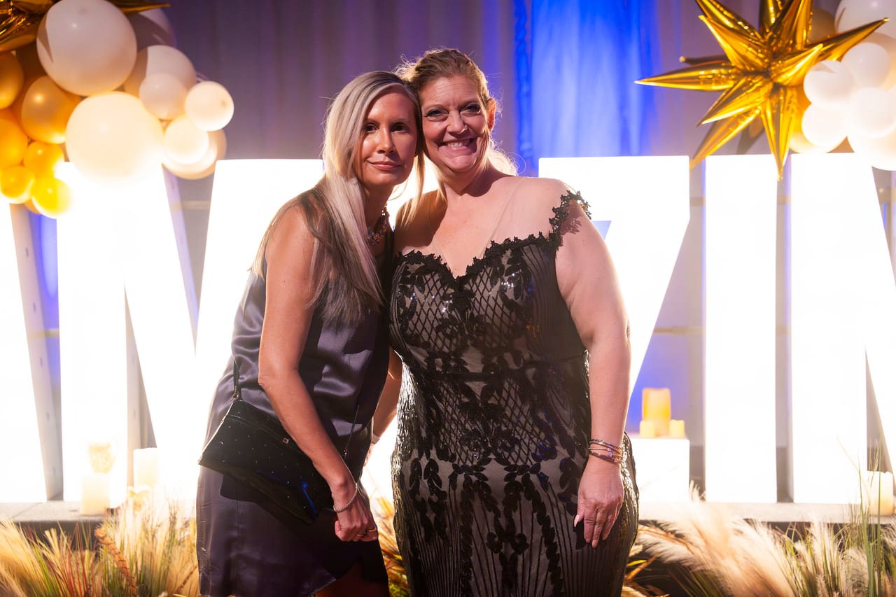 Two Renown friends cheek to cheek in front of the lit letters