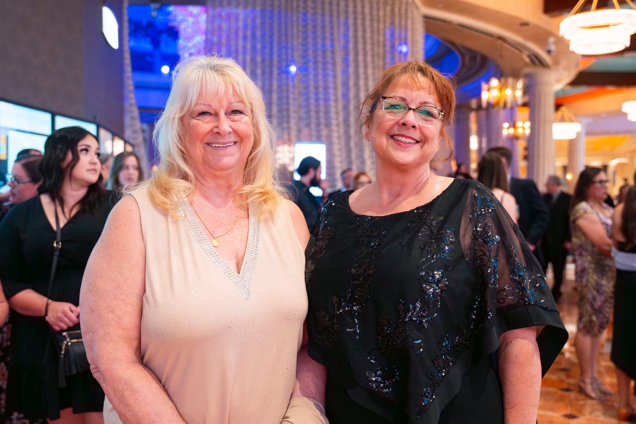 Two Renown friends dressed up and smiling in the busy Peppermill lobby
