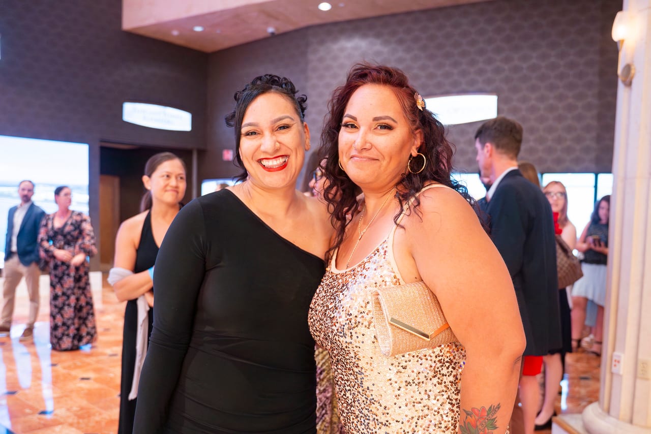 Two Renown friends smiling big in the hallway, one in a sequined dress