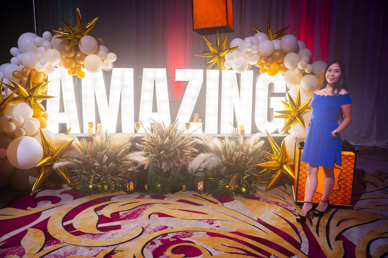 A Renown guest in a blue dress smiling beside the Amazing letters