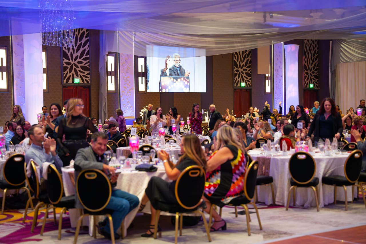 Renown guests cheering at their tables while a speaker appears on the screen