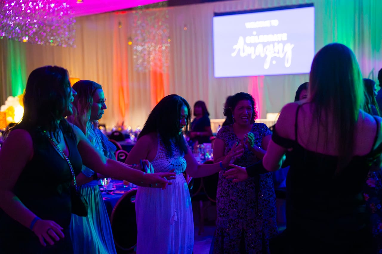 Renown guests dancing by their tables under the Celebrate Amazing welcome screen