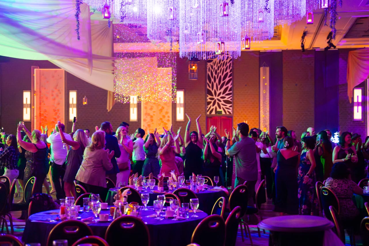 Renown guests dancing with their hands up under the crystal chandeliers