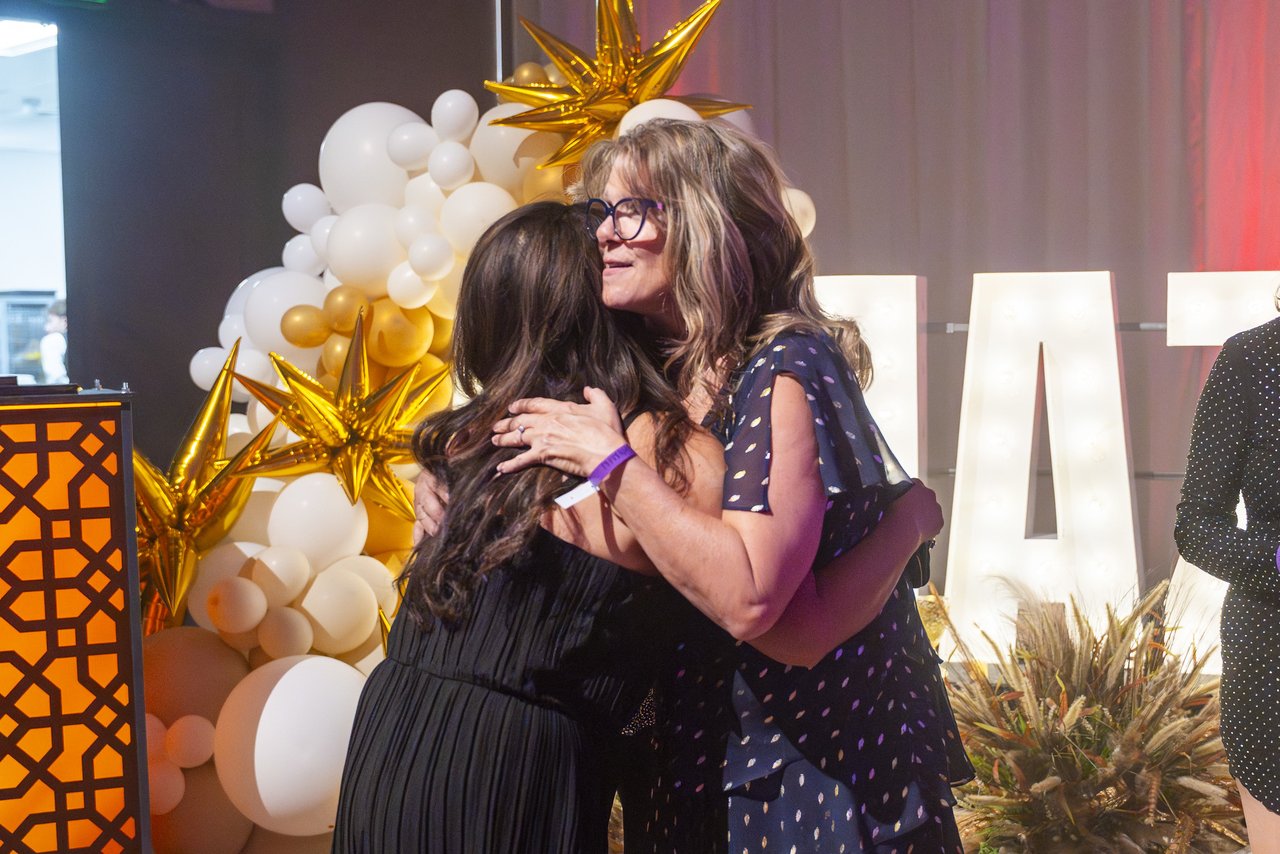 A Renown honoree hugging a friend beside the Amazing letters