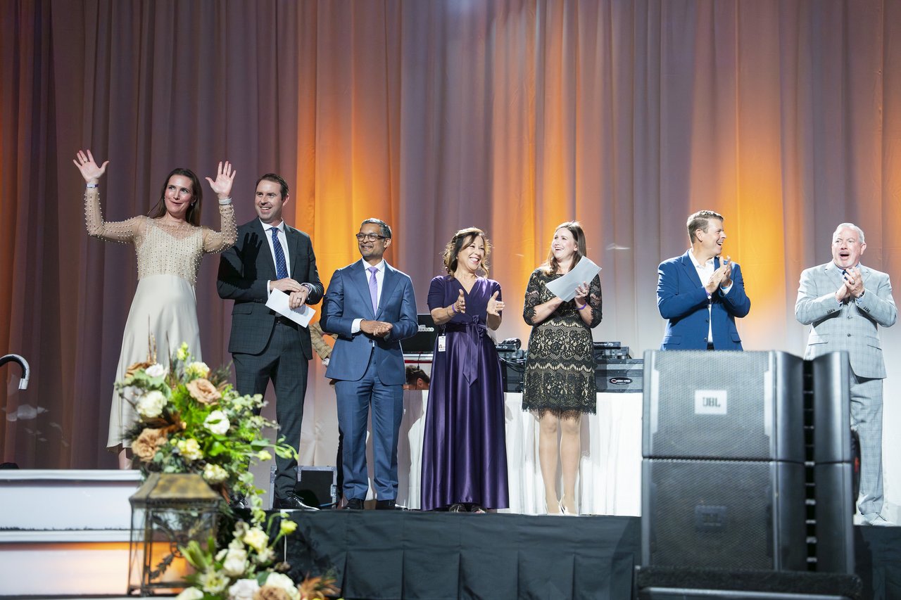 A Renown honoree waving both hands on stage beside the leaders