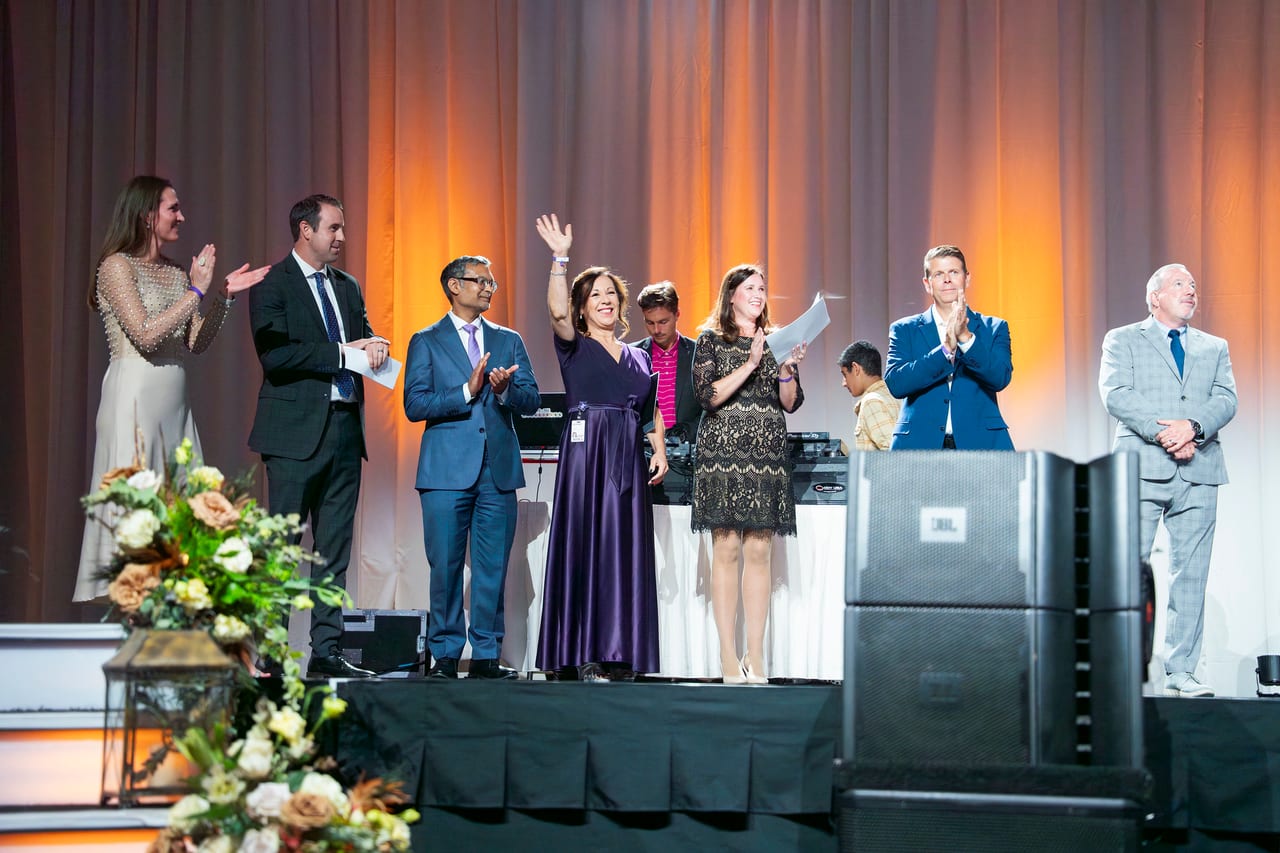 A Renown honoree waving to the room as leaders applaud on stage