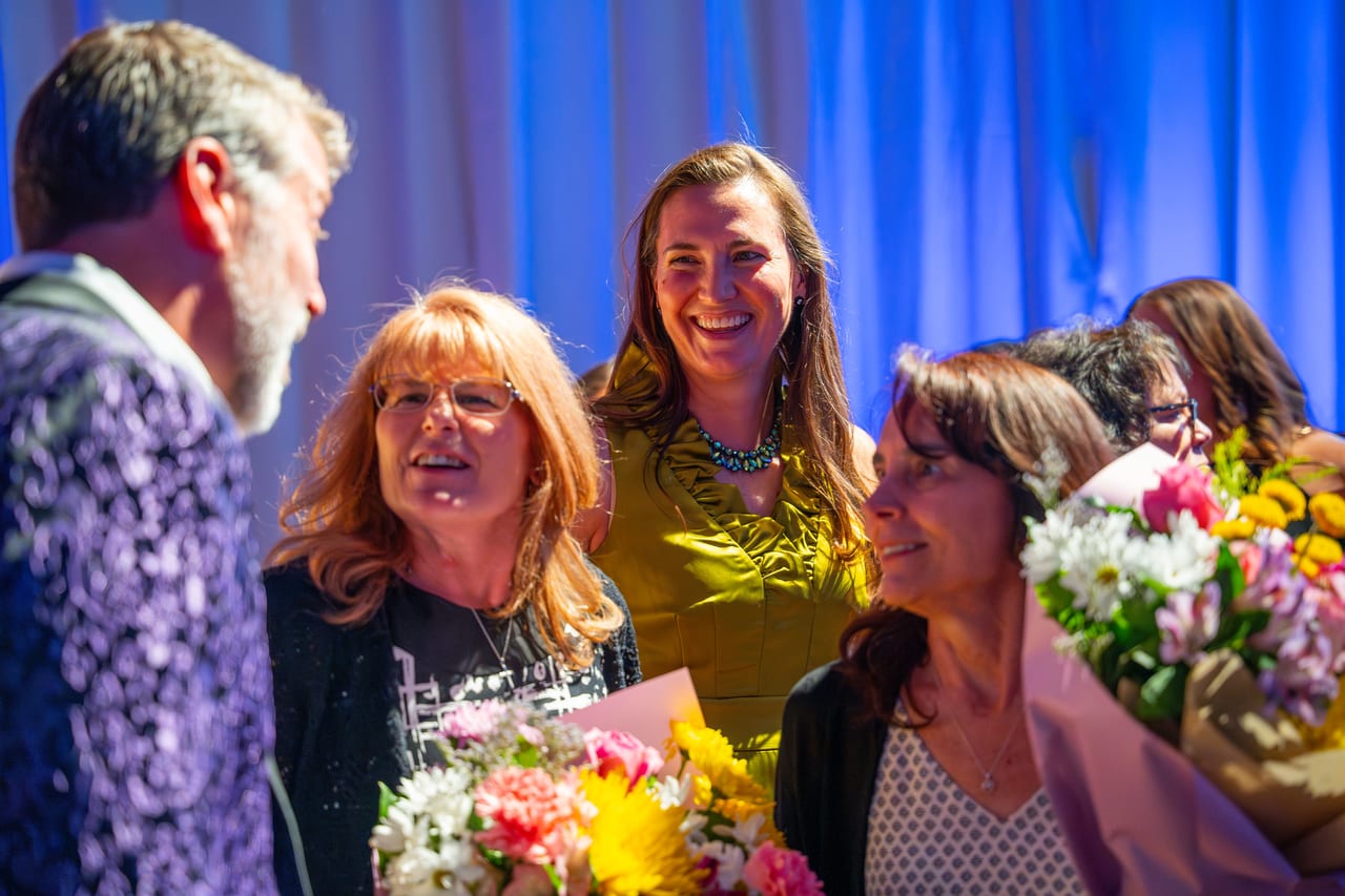 Renown honorees laughing with their flowers as the emcee congratulates them