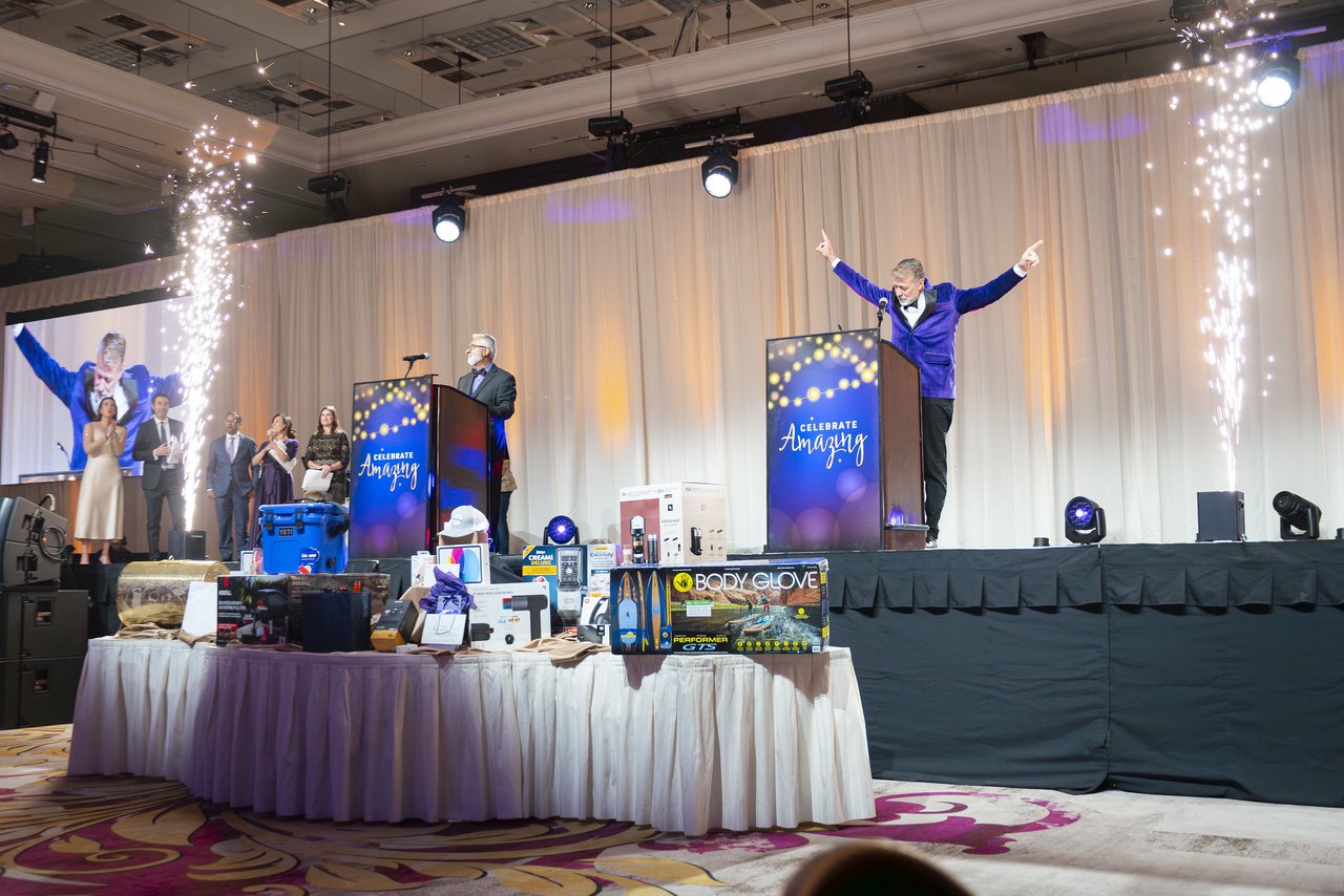 The host with his arms up on stage between the cold spark fountains