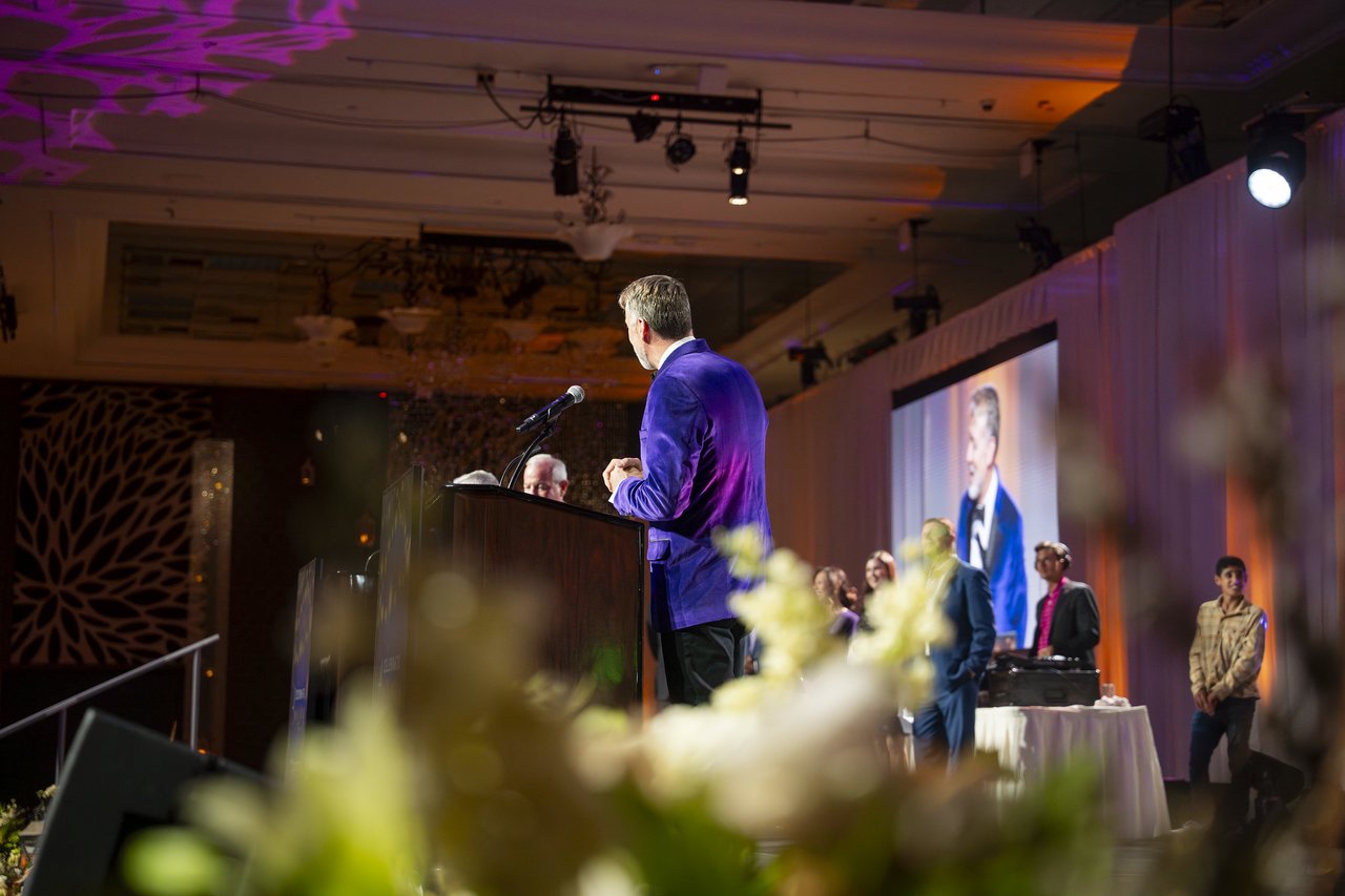 The host at the podium seen past the stage flowers