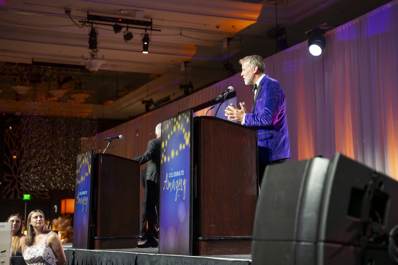 The host speaking at the Celebrate Amazing podium beside the big speakers