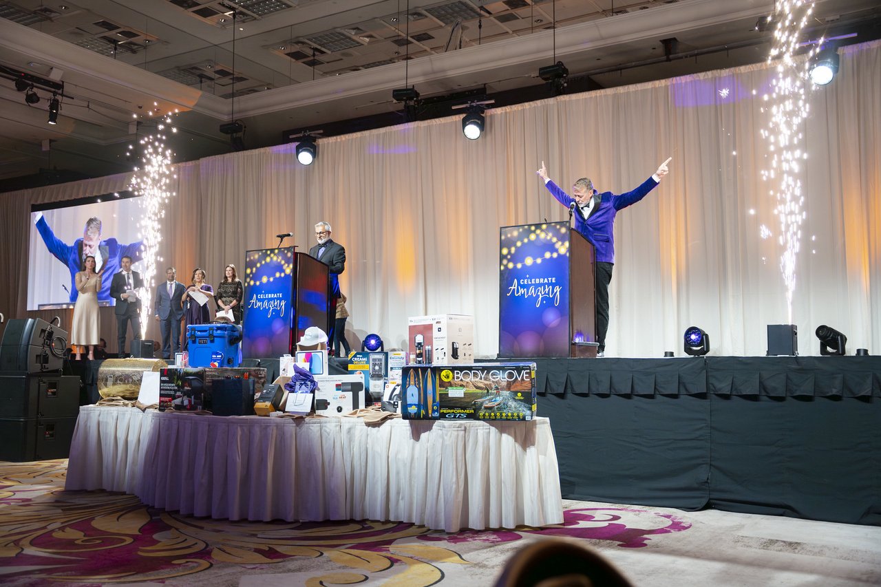 The host throwing his arms up on stage between the cold spark fountains