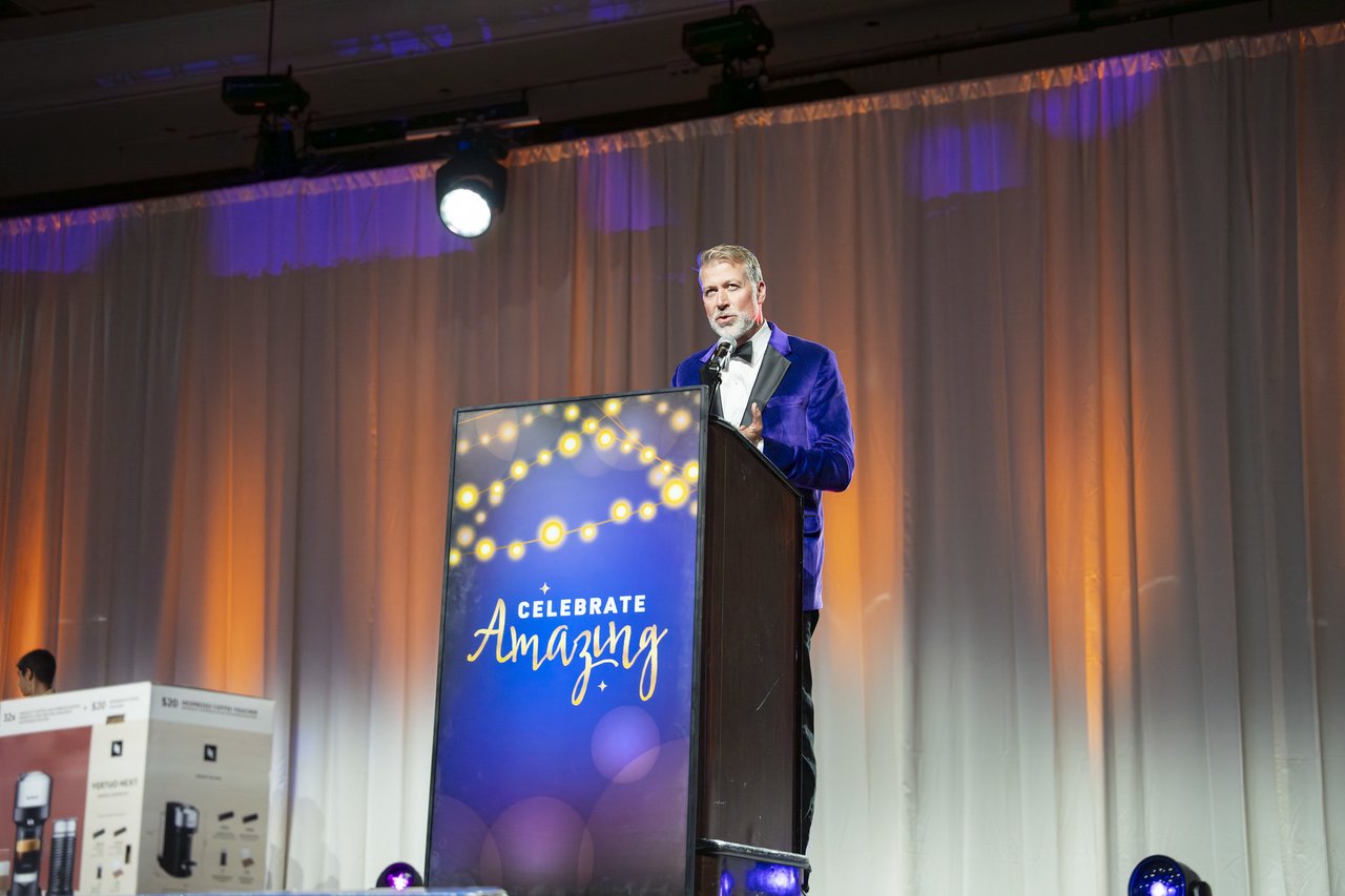 The host in a blue velvet jacket at the podium
