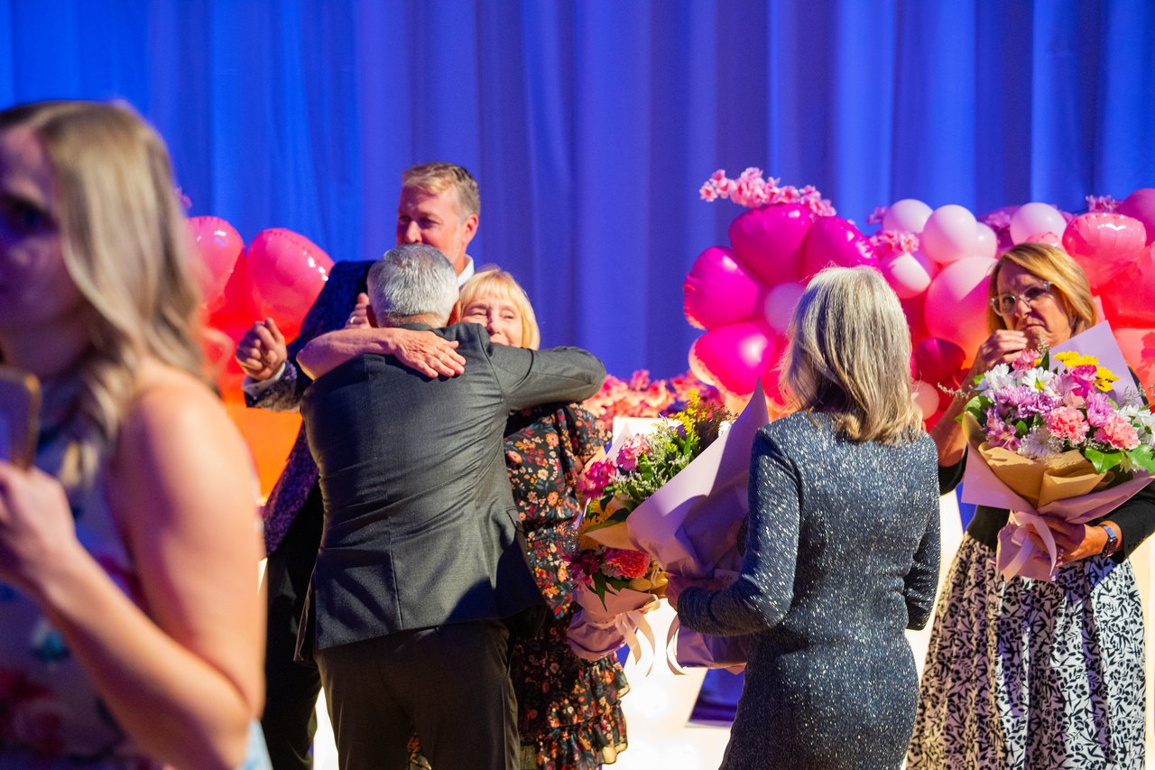 Renown coworkers hugging and holding bouquets by the balloon wall