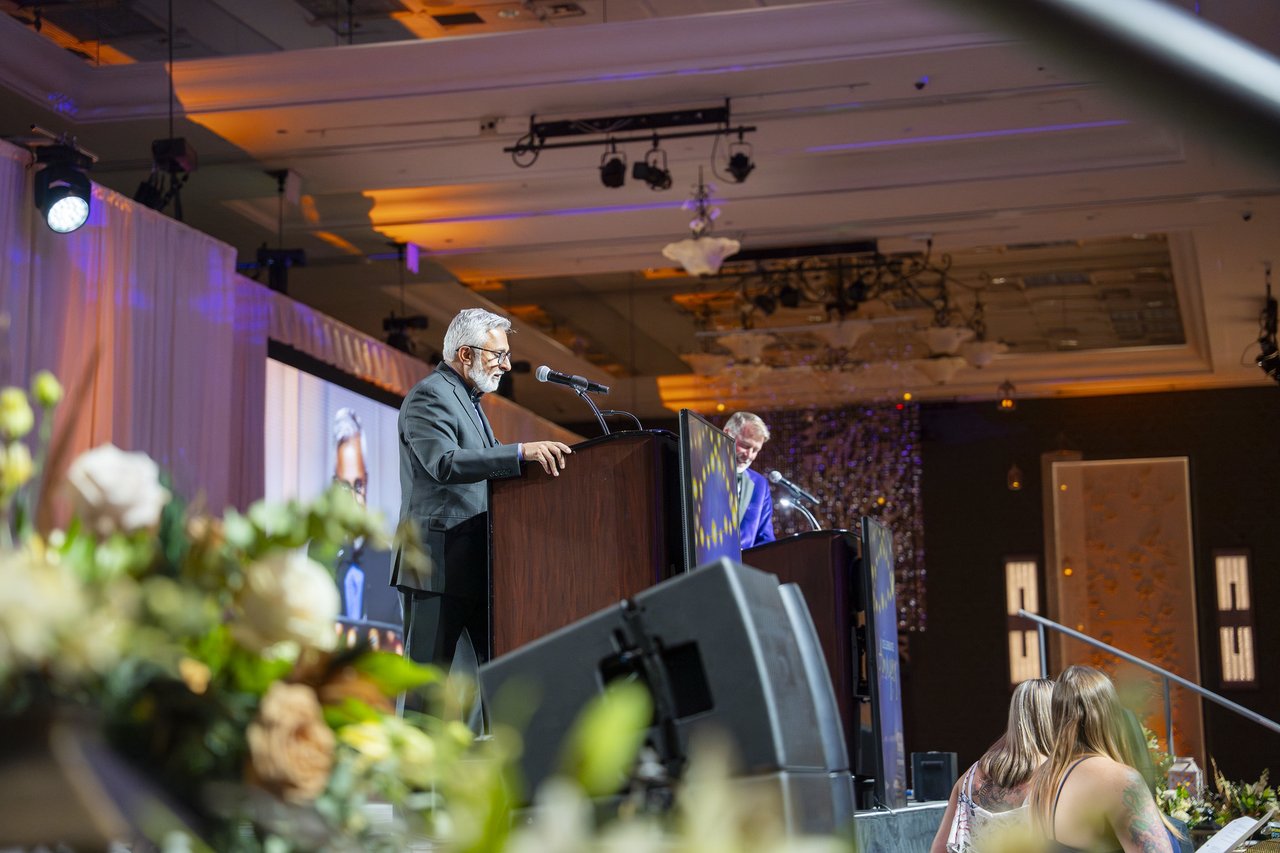 A Renown leader at the podium seen from behind the stage flowers