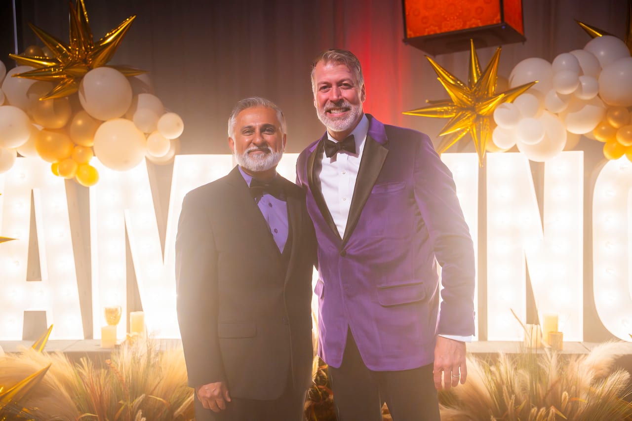 Two Renown leaders in tuxedo jackets smiling at the glowing letters