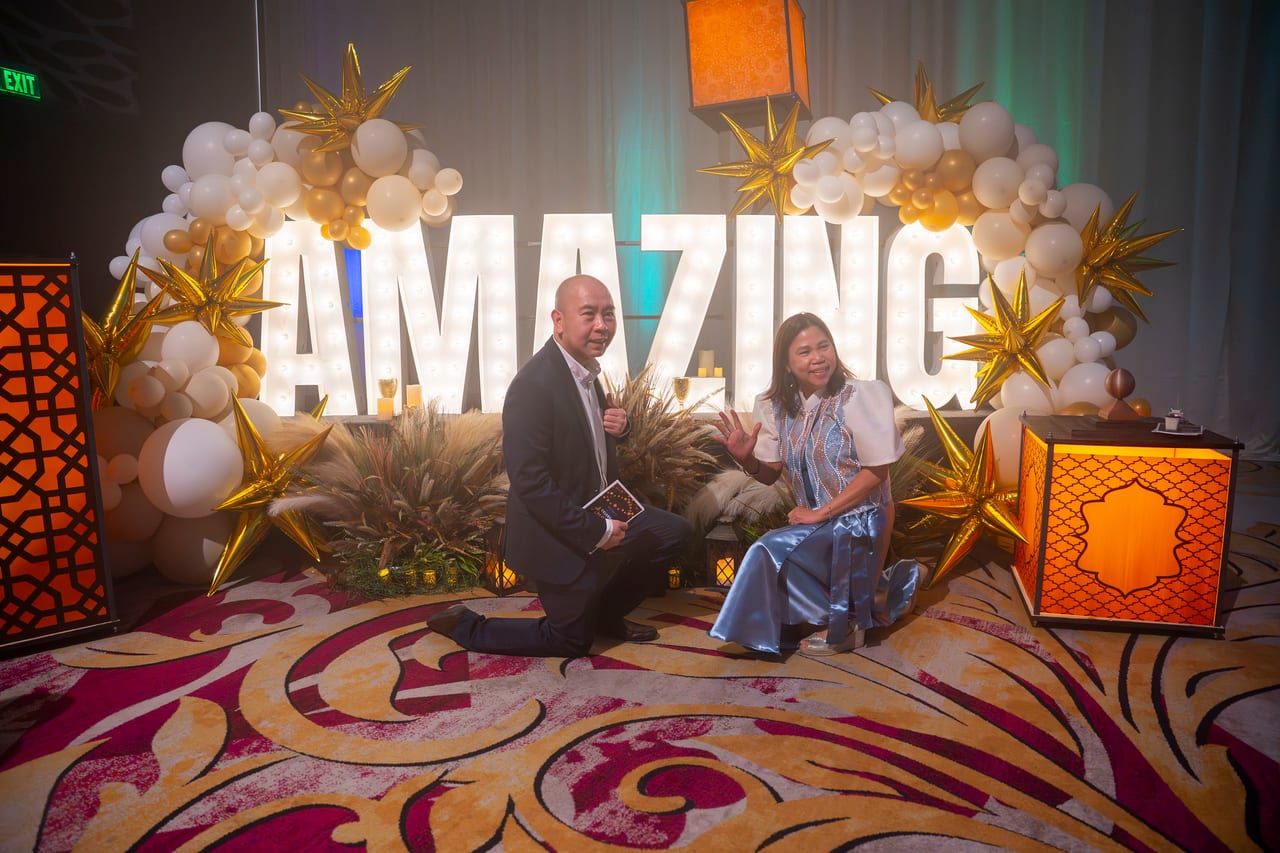 Two Renown guests kneeling playfully in front of the lit AMAZING letters