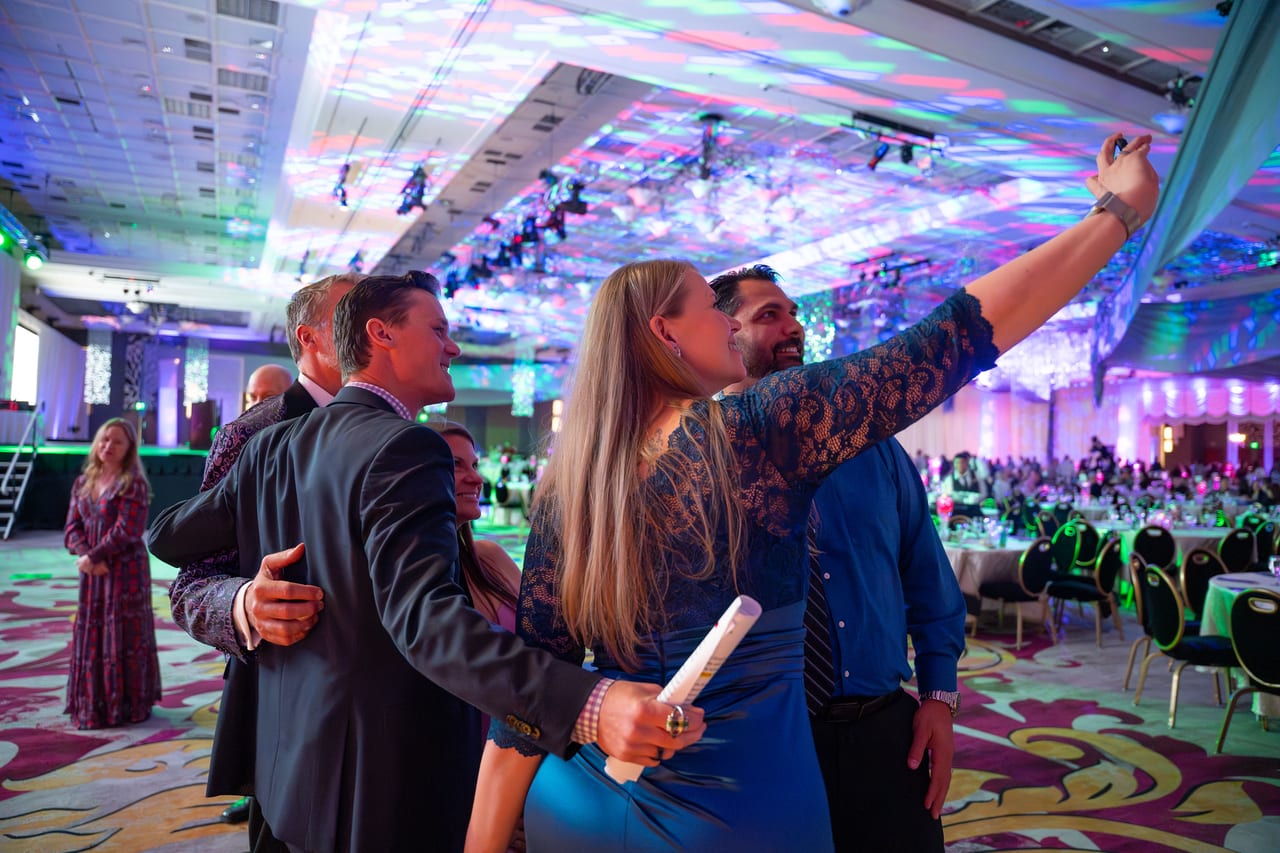 Renown coworkers squeezing in for a selfie with the ballroom lights behind them