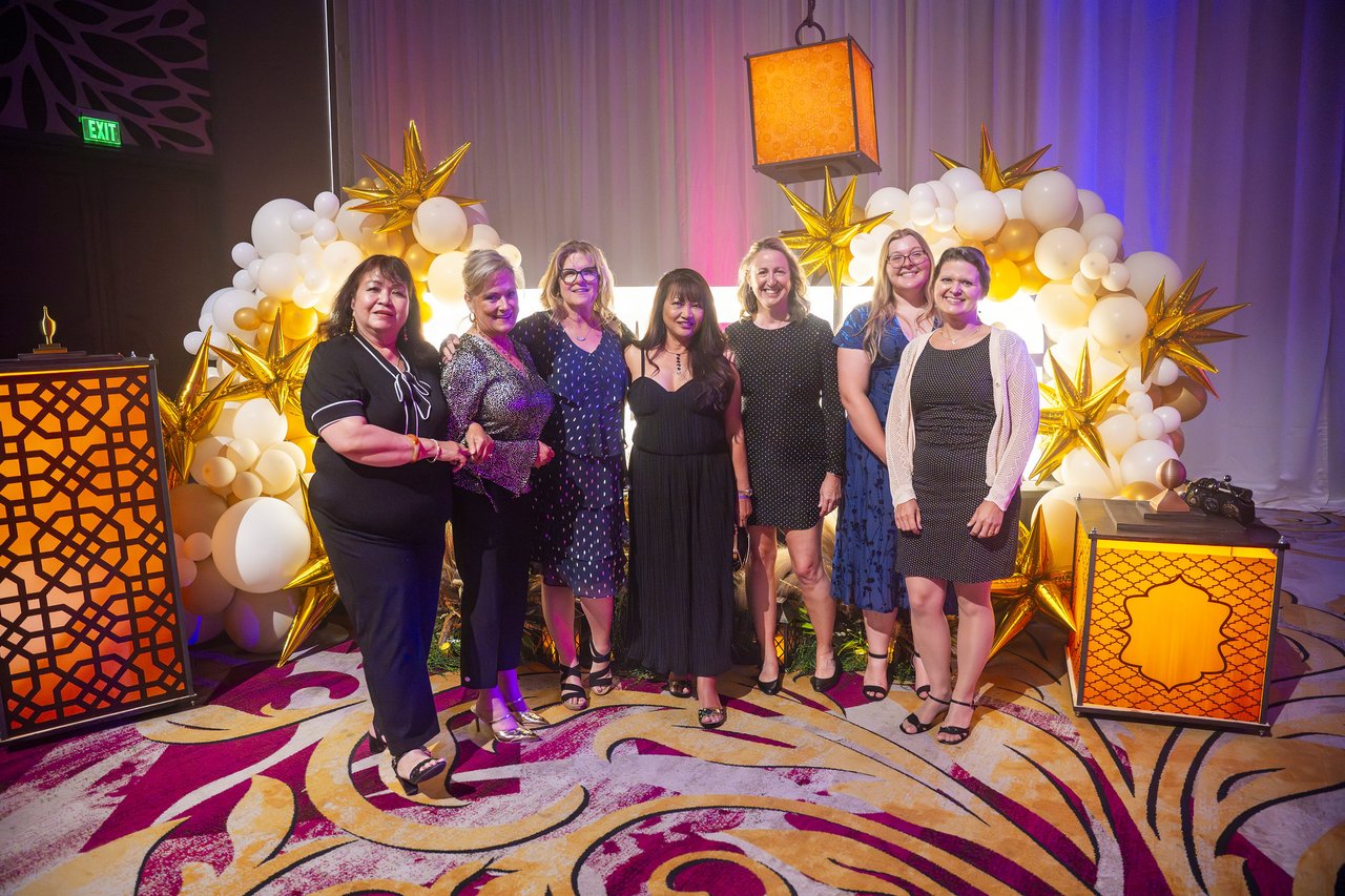Seven Renown coworkers posing at the gold balloon arch
