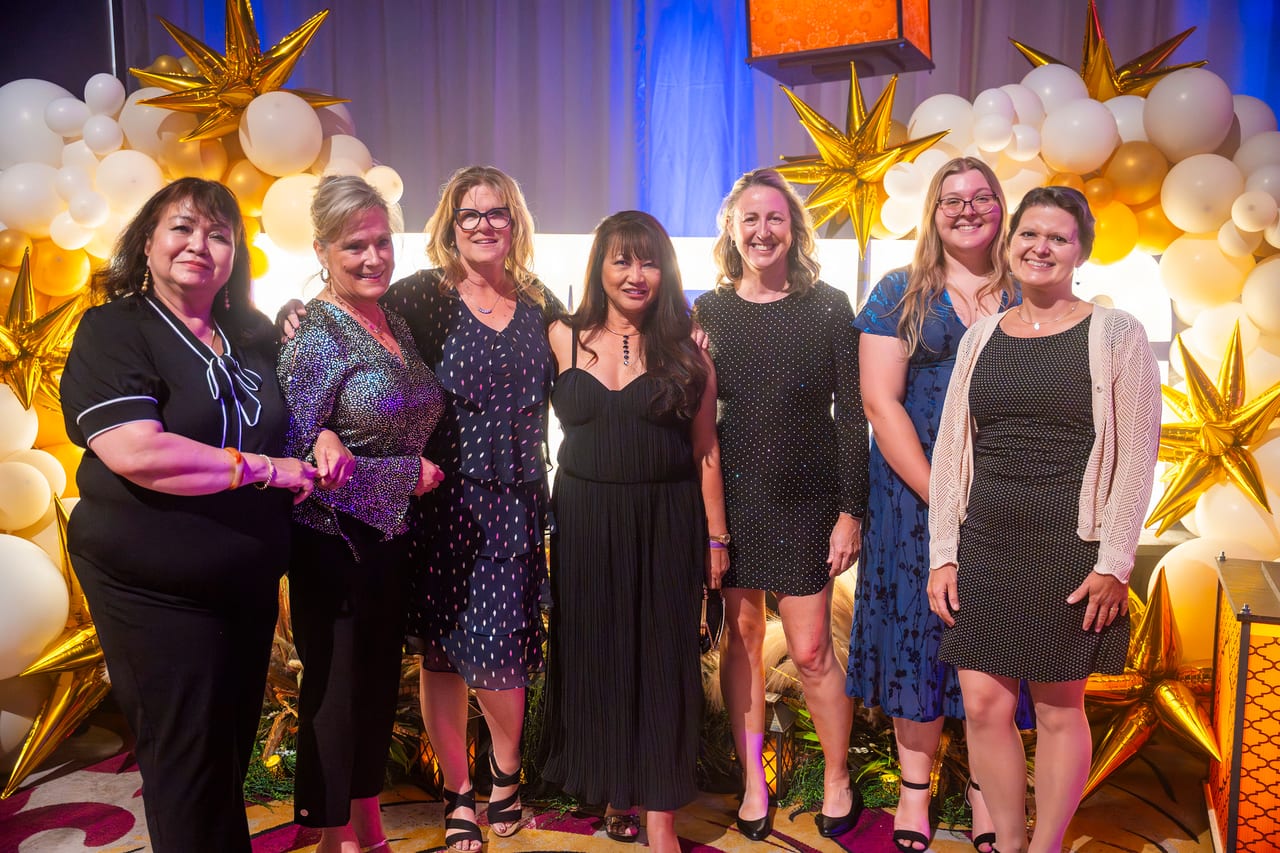 Seven Renown coworkers standing together at the gold star balloon wall