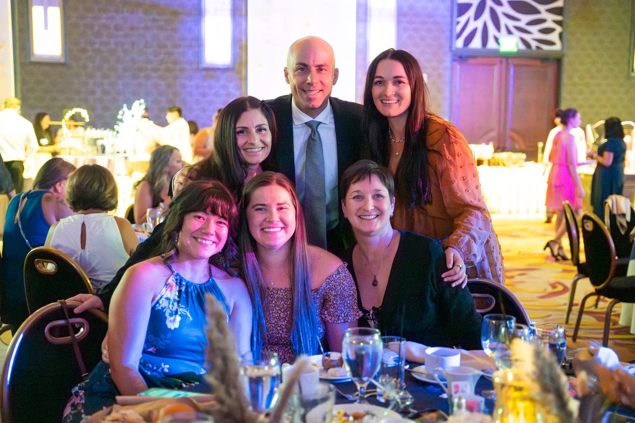 Seven Renown friends crowding in for a photo at their table