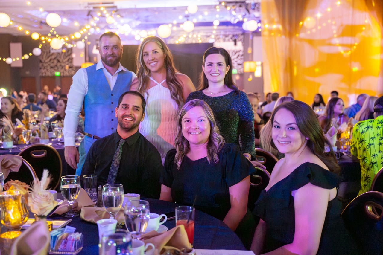Six Renown friends gathered around their table under the string lights