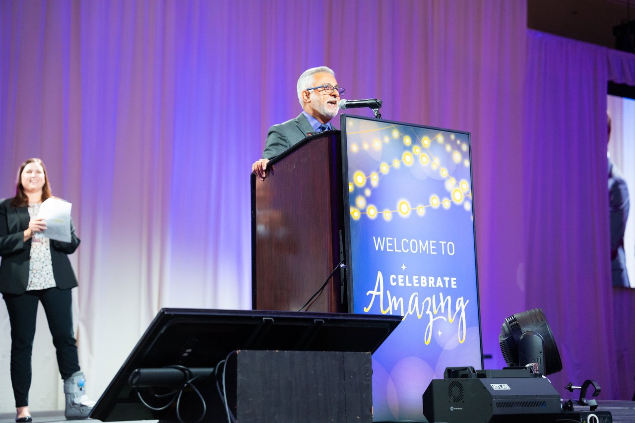 A Renown speaker at the Celebrate Amazing podium as a presenter waits