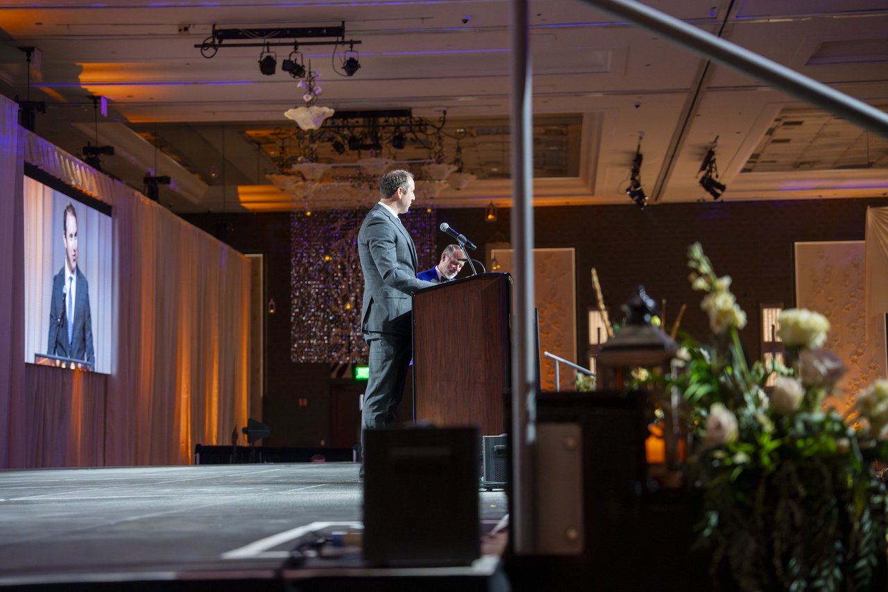 A Renown leader speaking from the podium with his face on the screen