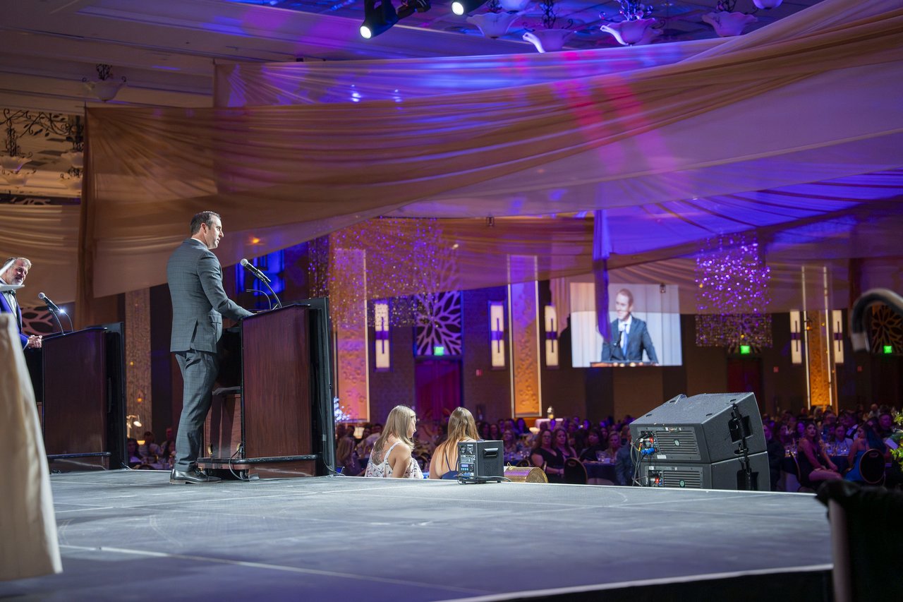 A Renown leader speaking from the wide stage with his face on the screen
