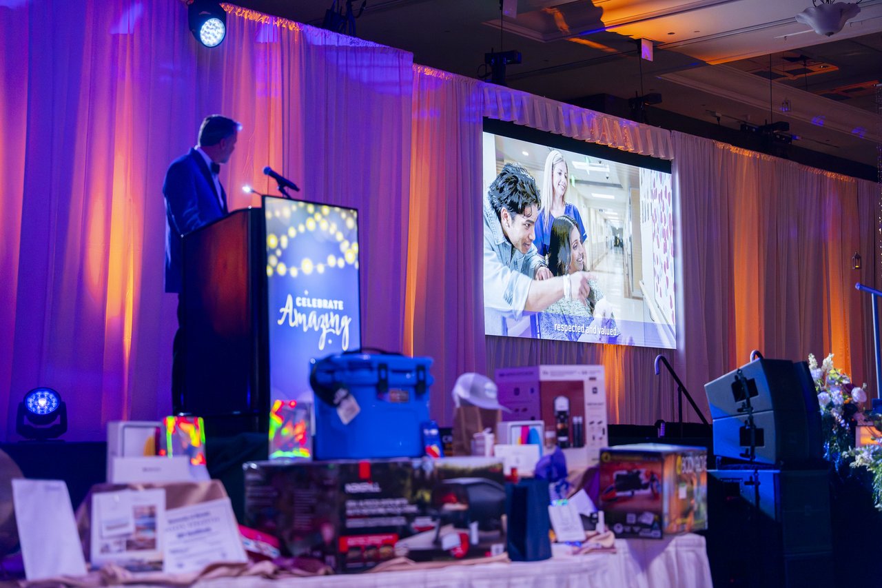 A Renown leader at the podium with a care team video on the big screen