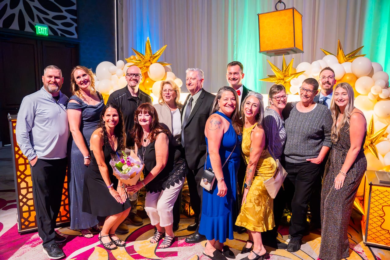 A big Renown team gathered at the gold balloon wall, one holding a bouquet