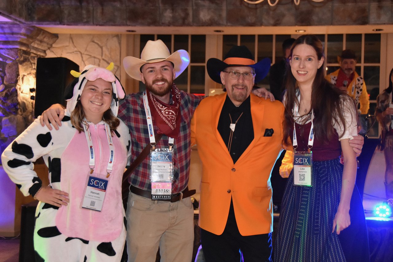 A costumed group in a cow suit, cowboy hats and an orange jacket by the dance floor