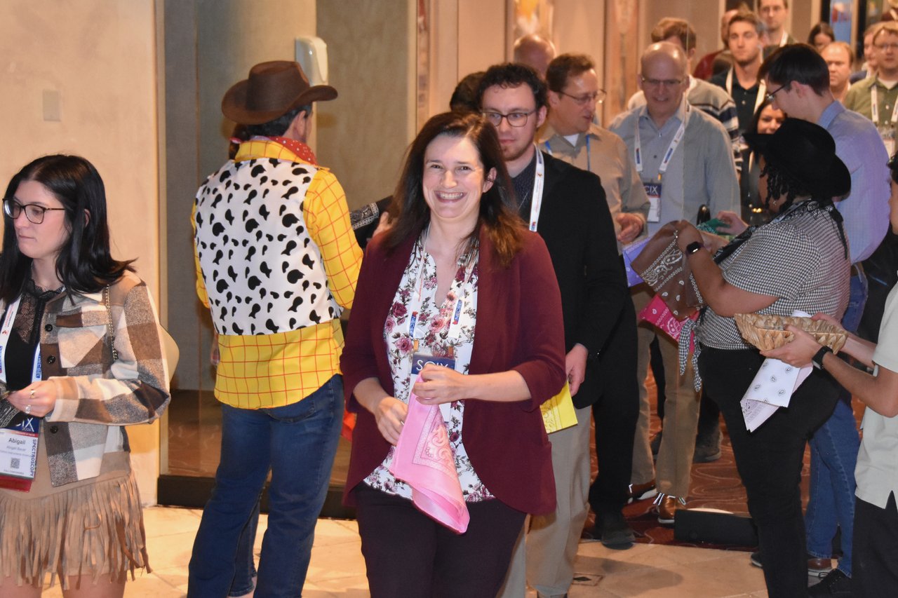 A greeter in a cowboy hat and cow print vest handing out bandanas at the SciX Gala