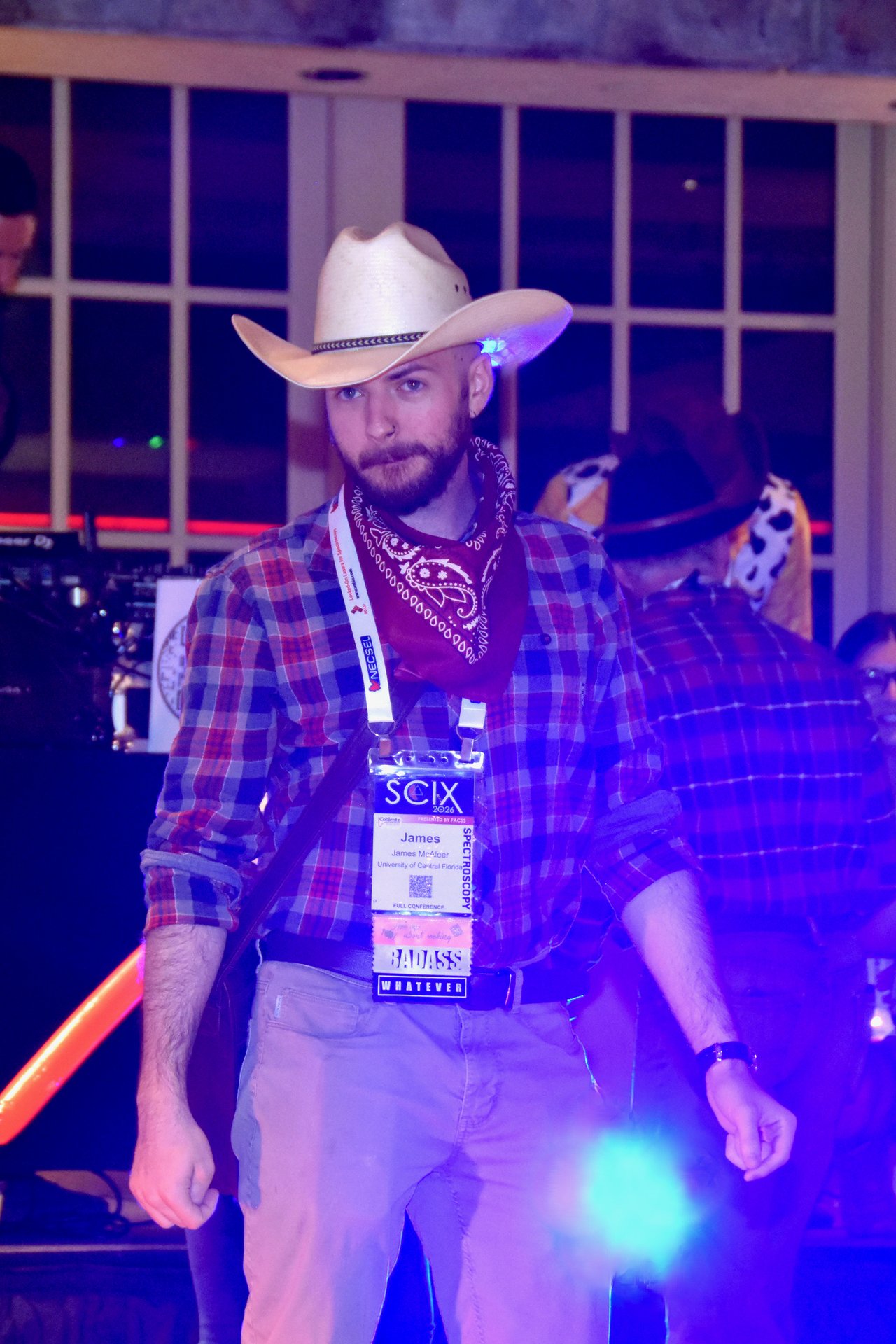 A guest in a cowboy hat and bandana under purple dance lights