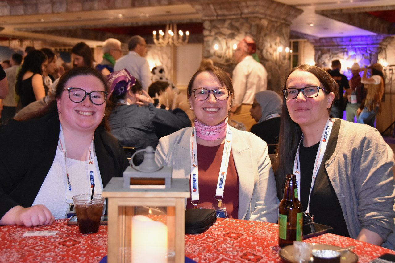 Three SciX Gala guests smiling at a table with a red bandana cloth and a lantern