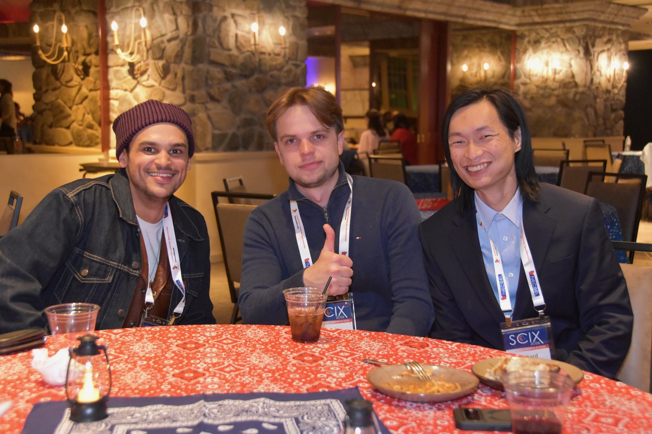 Three SciX Gala guests at a red bandana table, one giving a thumbs up