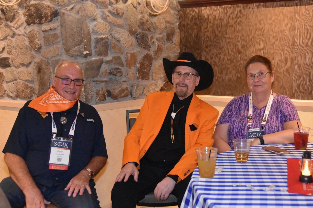 Three SciX Gala guests in western wear seated by a checkered table